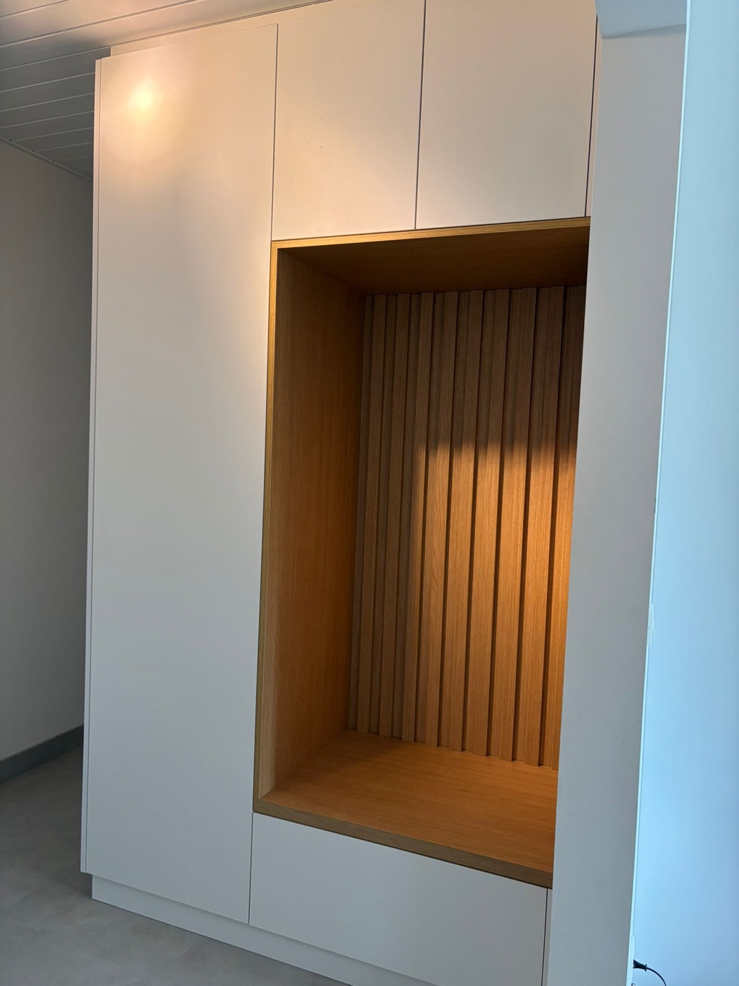 Dezelfde gang na de plaatsing: een witte kastwand met eiken zitnis en lattenwand