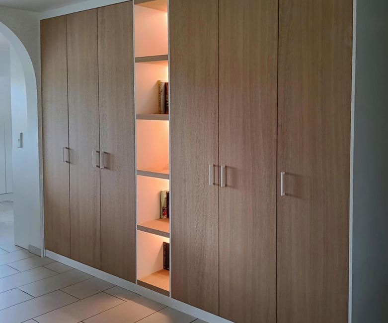 Hoge gangkast in donker hout, van vloer tot plafond, met verlichte open vakken